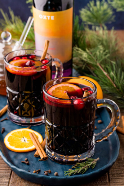 two glasses of mulled wine on a tray next to a bottle of red wine