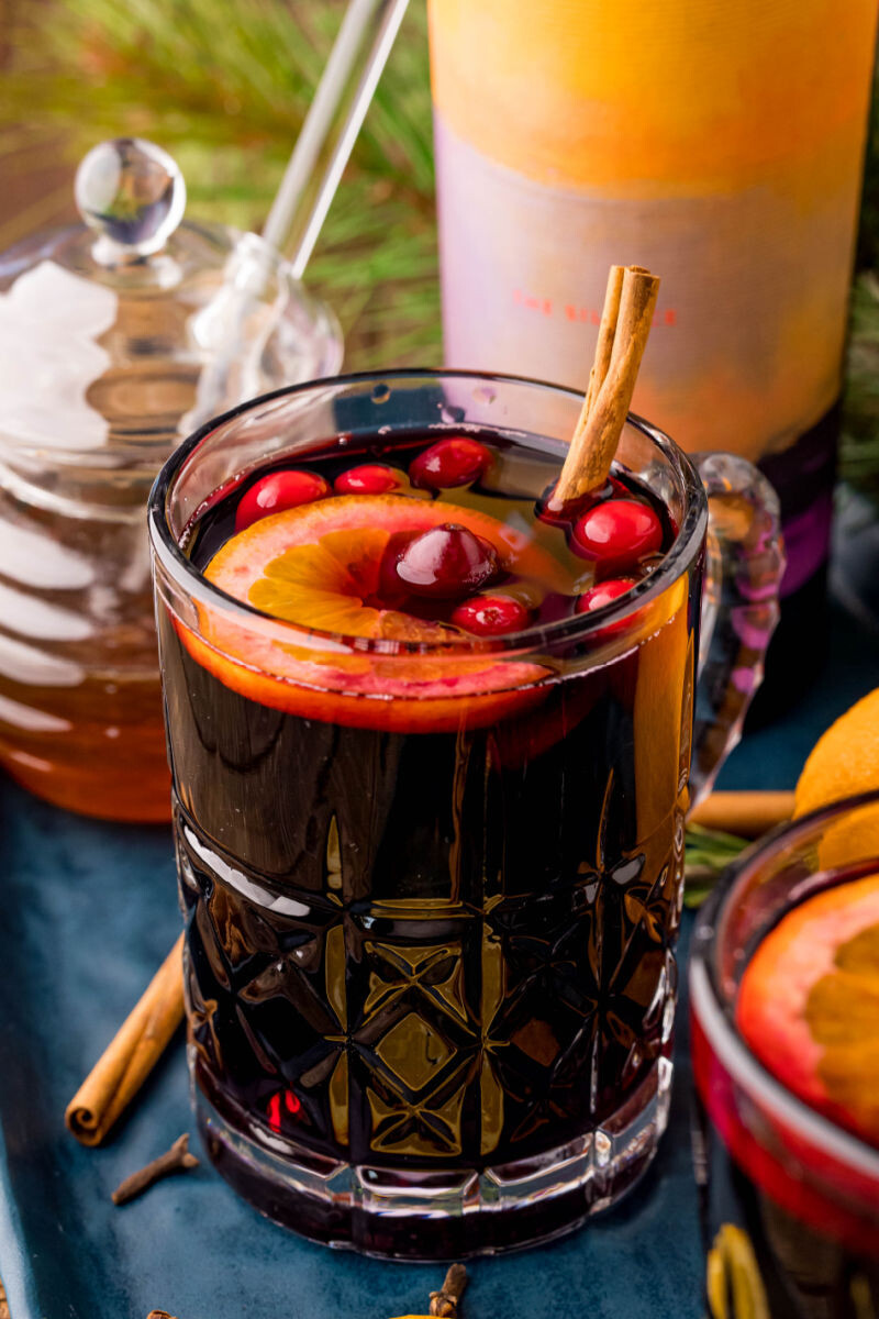 mulled wine in a glass mug next to a jar of honey and bottle of wine