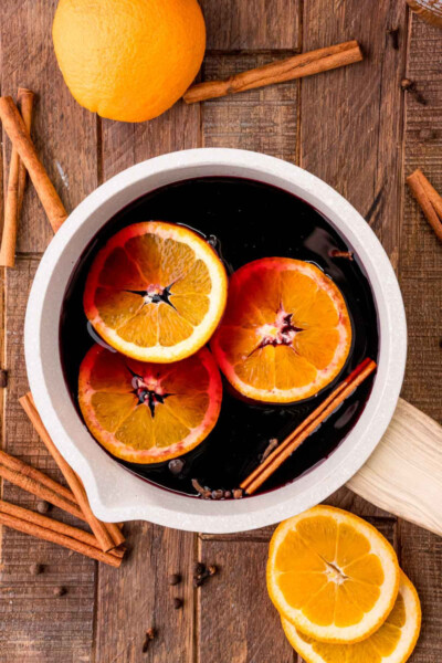 red wine, spices, and orange slices in a saucepan