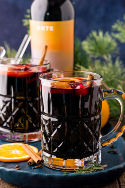 side view of mugs of mulled wine on a tray in front of a bottle for wine