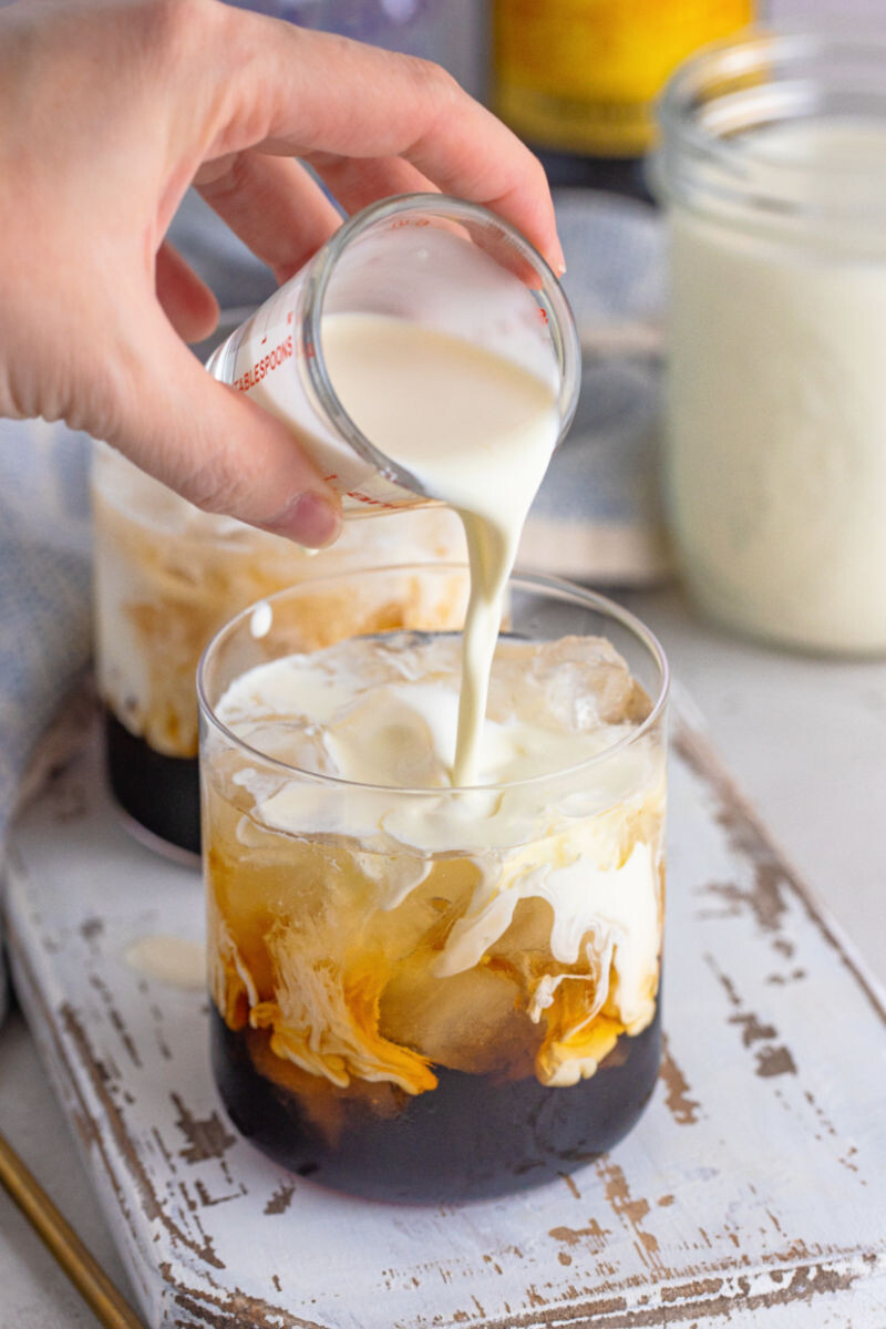 heavy cream being poured into a rocks glass with ice, vodka, and kahlua