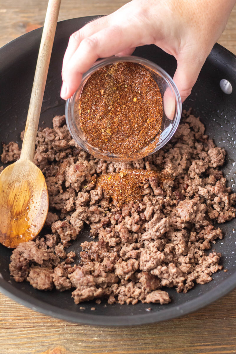 taco seasoning being added to cooked ground beef in a skillet