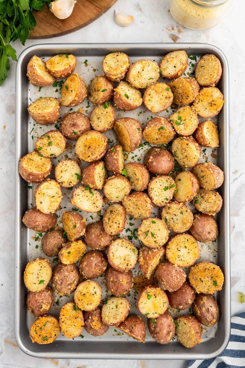 baked parmesan roasted red potatoes on a baking sheet with chopped parsley sprinkled over top