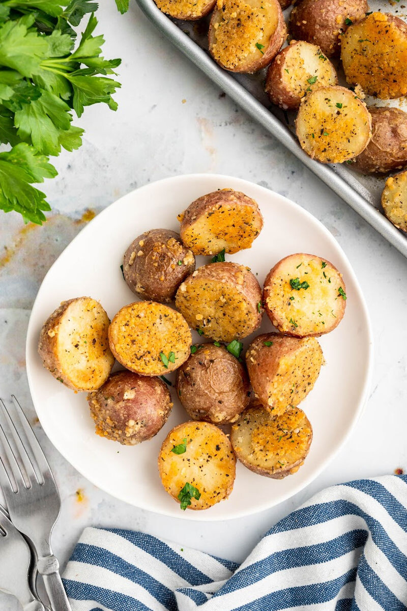 baked parmesan red potatoes on a plate next to the baking sheet