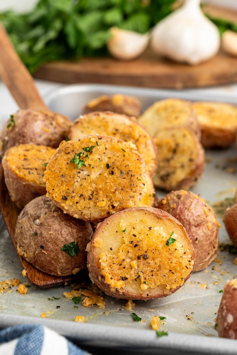 close up of baked parmesan red potatoes on a wooden spatula over the baking sheet