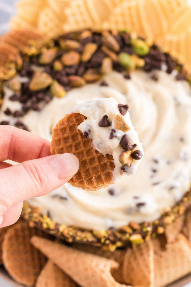 hand holding a mini stroopwaffle that's been dipped in cannoli dip