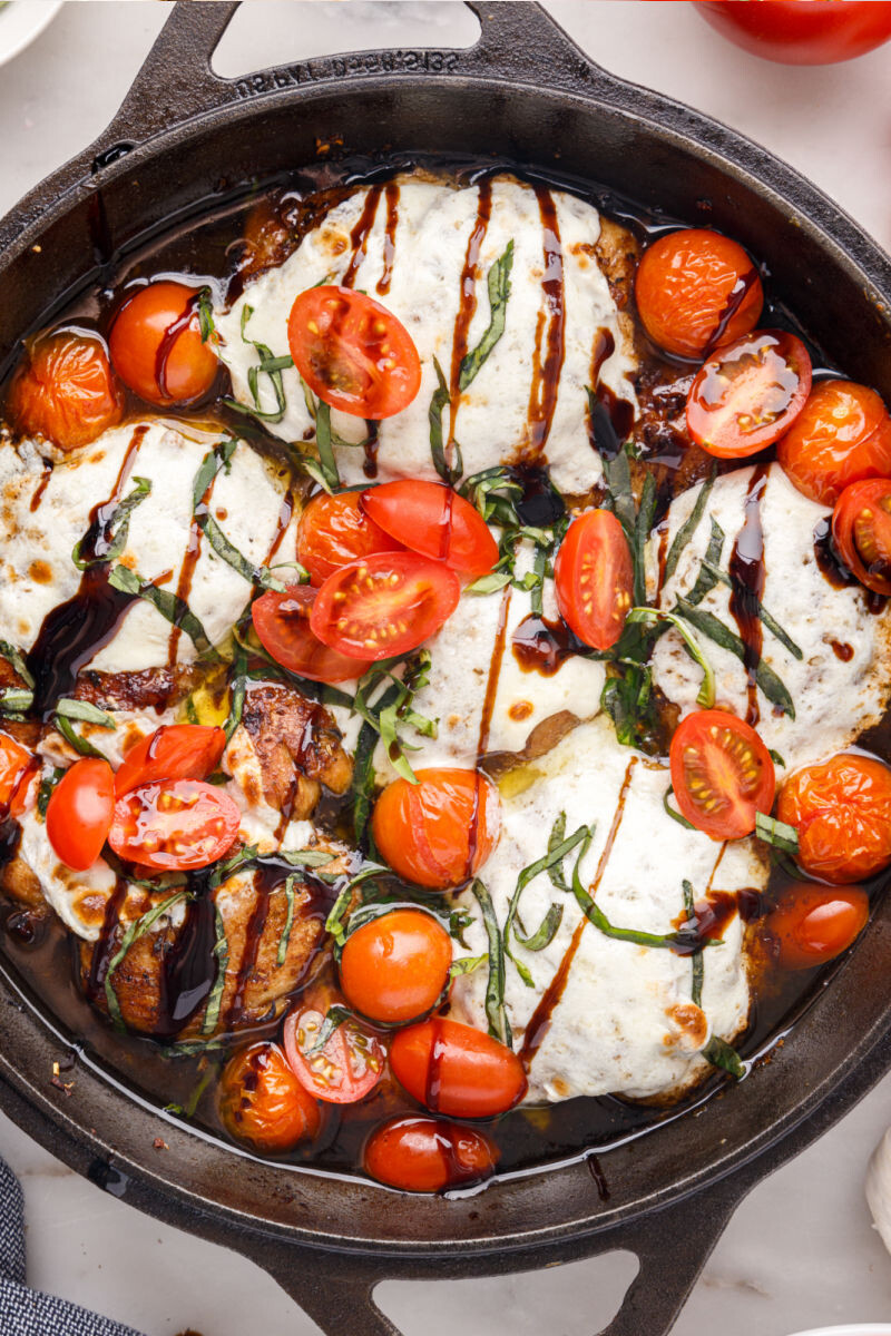 caprese baked chicken thighs topped with balsamic glaze, halved cherry tomatoes, and basil