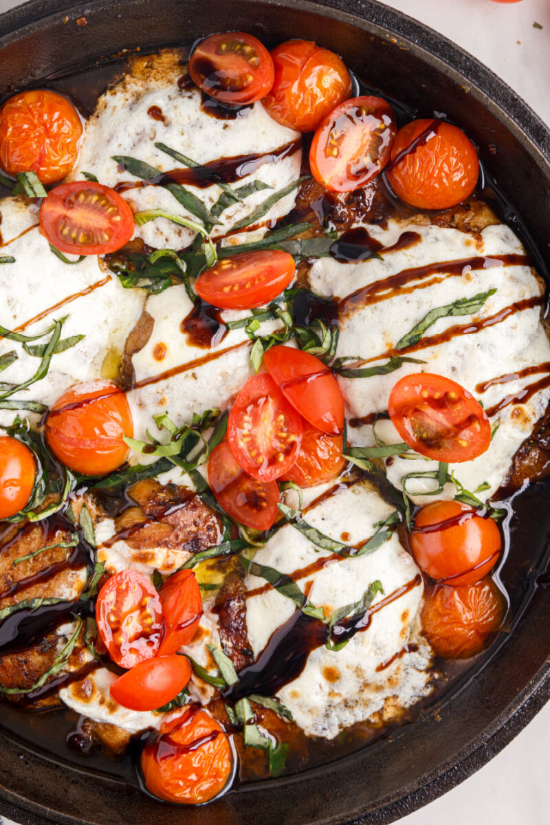 close up of caprese baked chicken thighs in a skillet with tomatoes, balsamic glaze, and basil on top