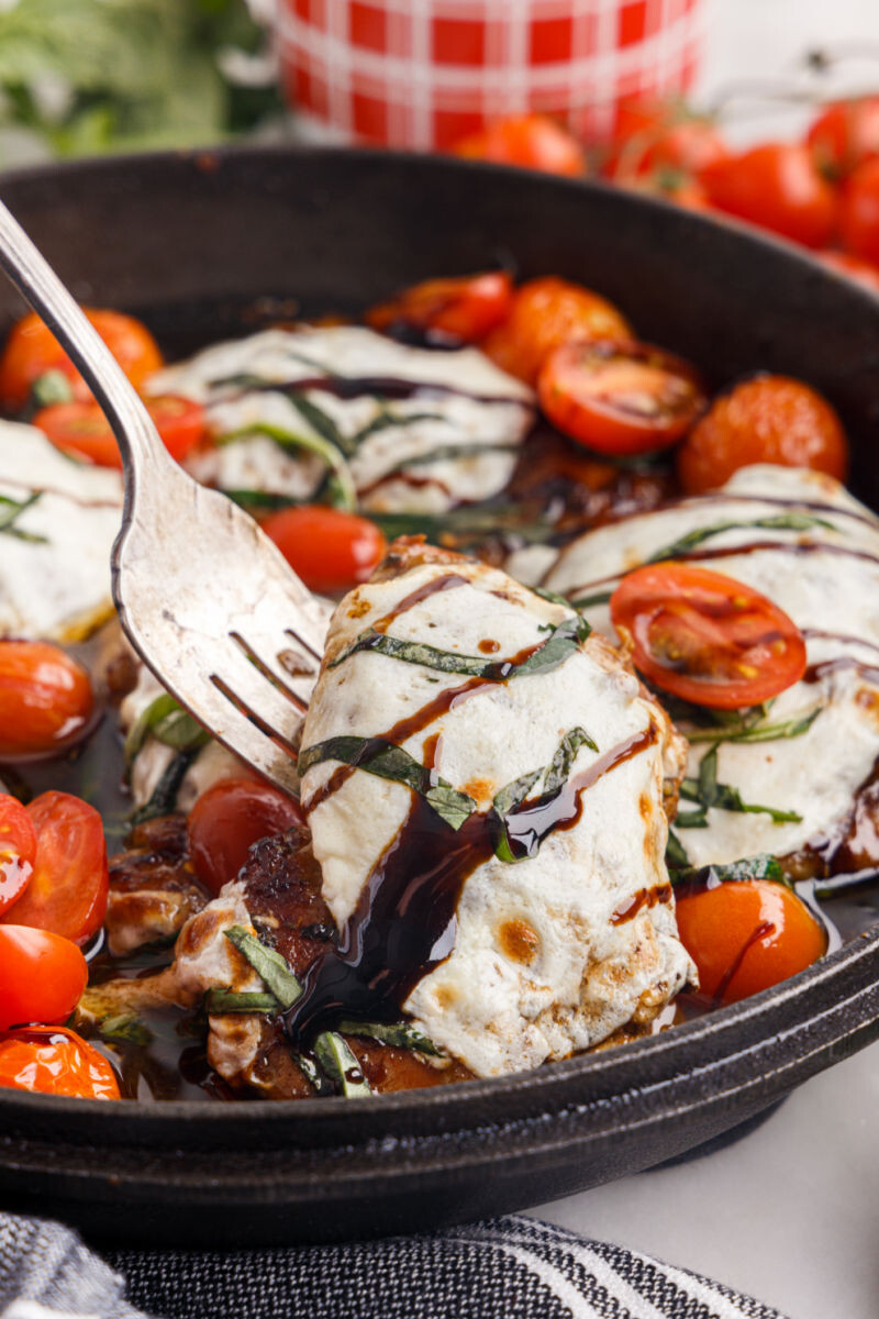 serving fork lifting a caprese baked chicken thighs from the skillet
