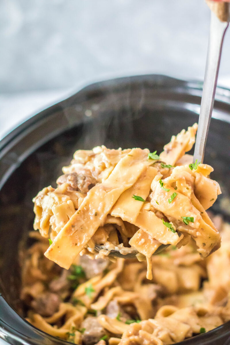 ladle of crock pot beef and noodles over the slow cooker