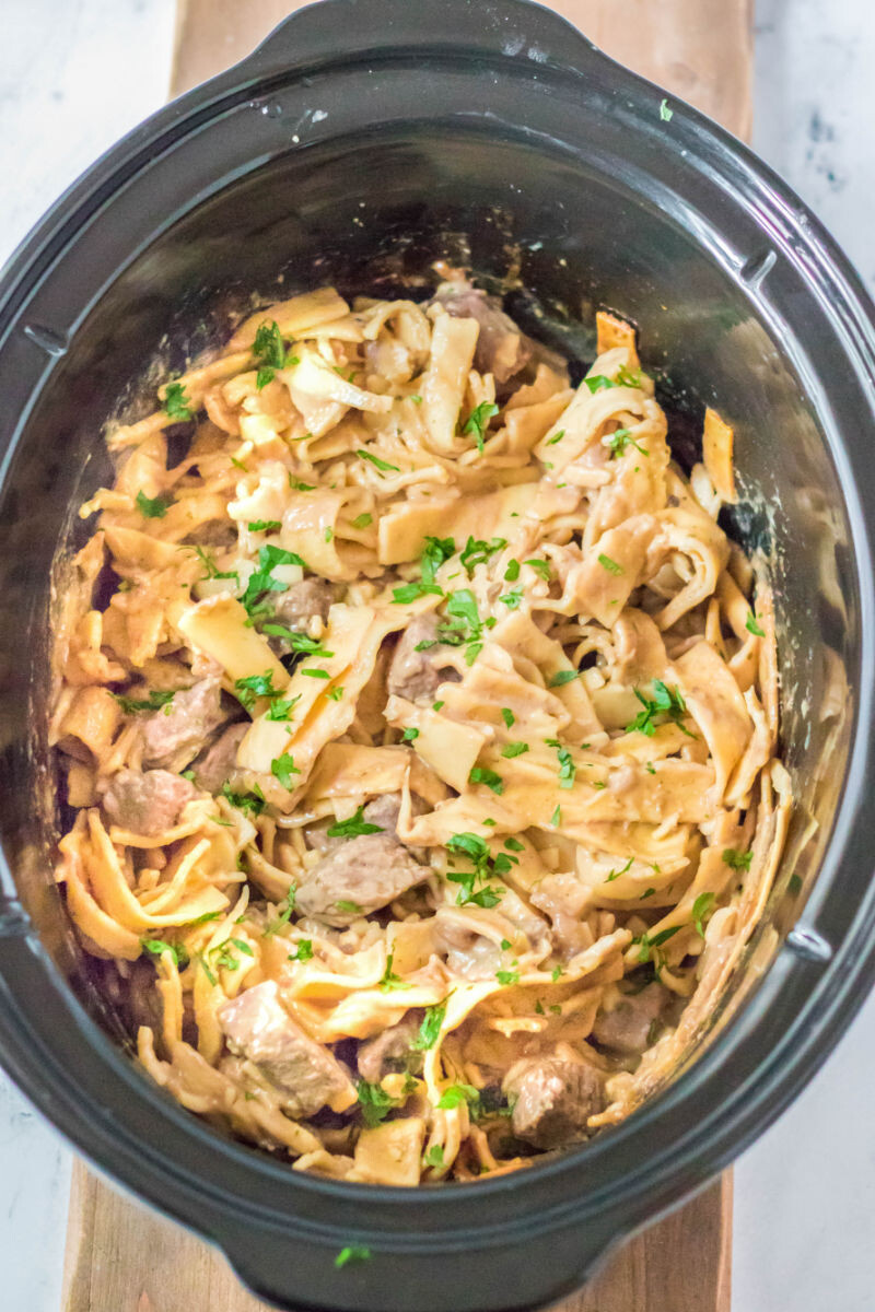 crock pot beef and noodles in a slow cooker with parsley sprinkled on top.