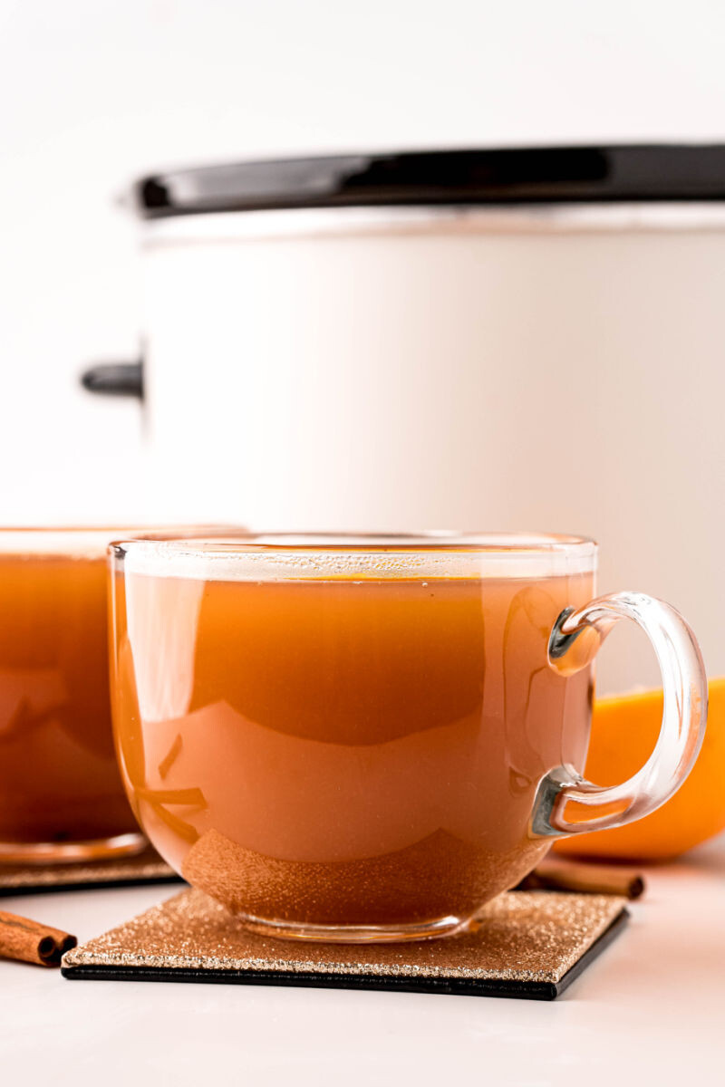 side view of mugs of crock pot mulled cider in front of a slow cooker