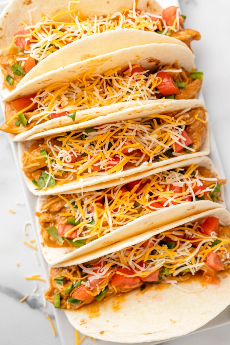 platter of crock pot queso chicken tacos with cheese, tomatoes, jalapeno, and cilantro