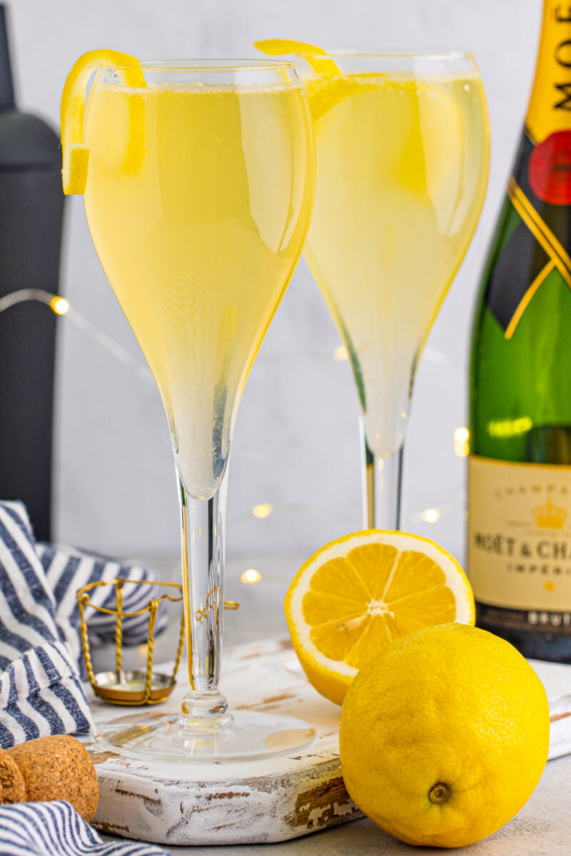 French 75 cocktail with a lemon twist in front of a bottle of champagne