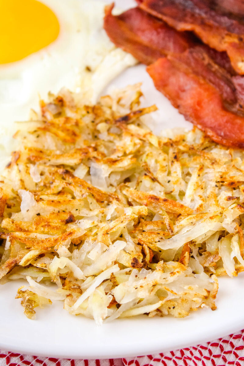 shredded hash browns on a plate next to bacon and eggs