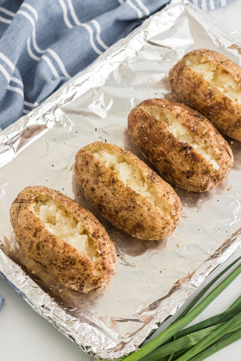 baked potatoes cut lengthwise on a foil lined baking sheet