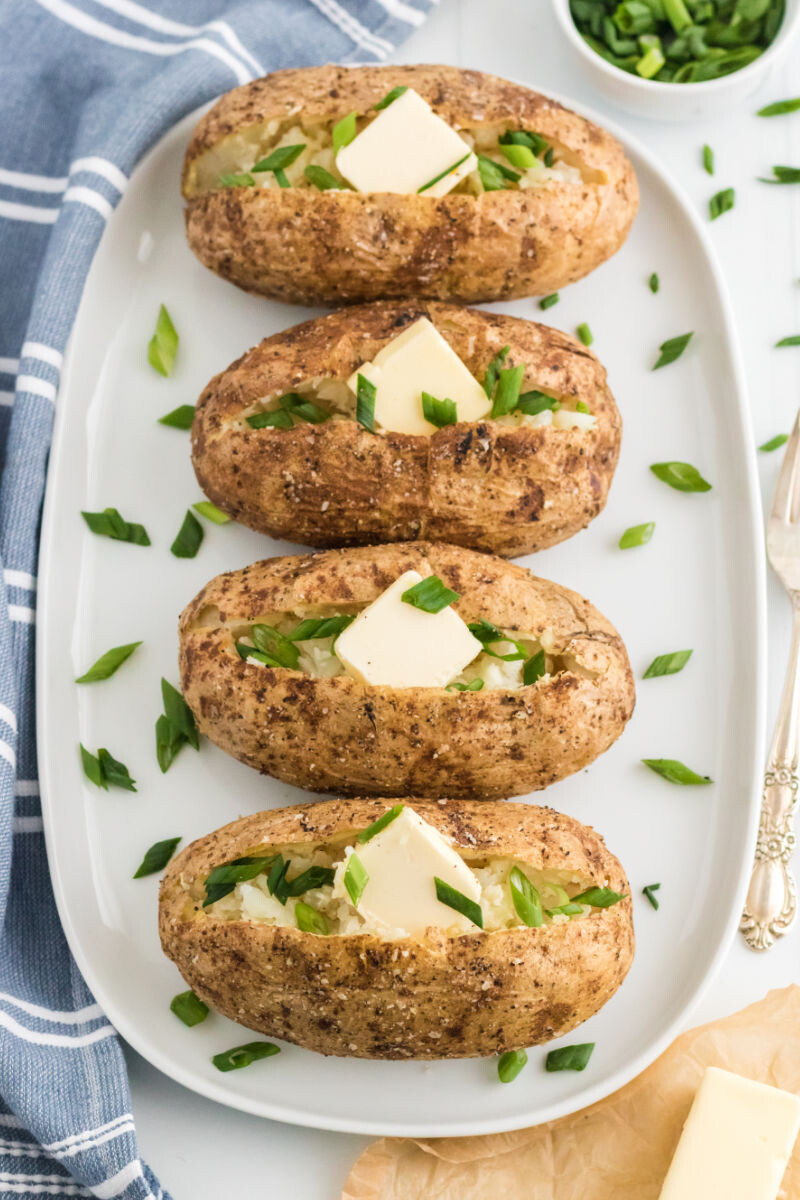 four baked potatoes with butter and green onions on a platter
