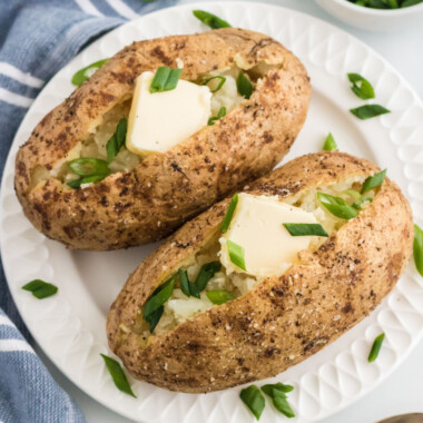 square image of two baked potatoes with butter and green onions on a plate