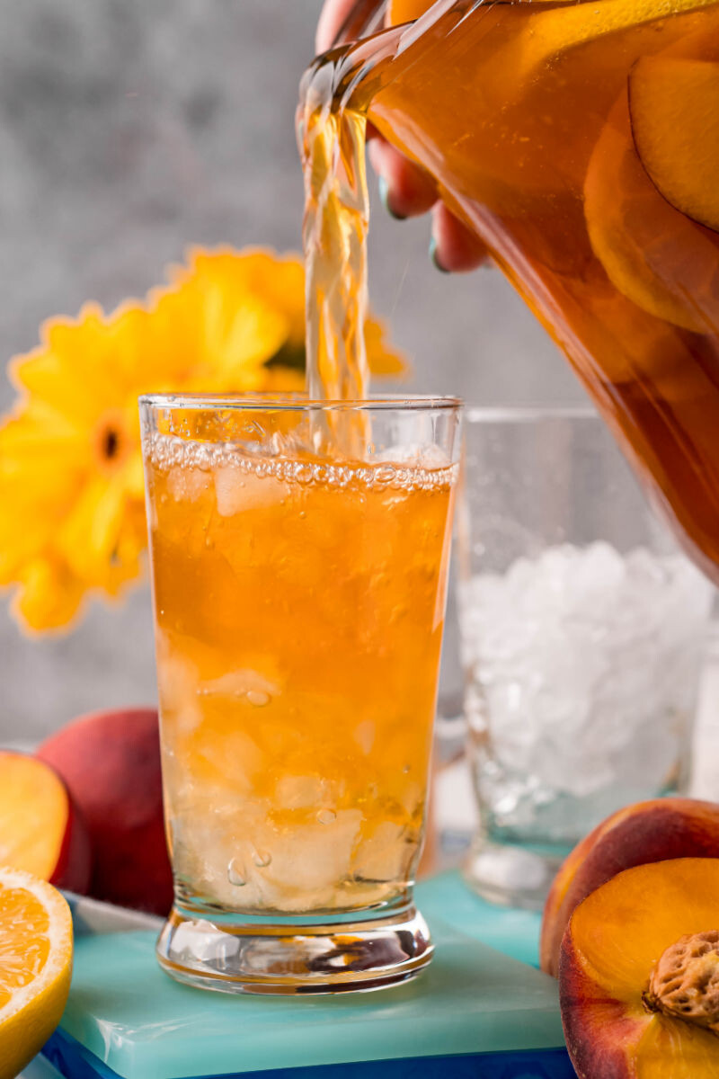 peach sweet tea being poured into a glass filled with ice