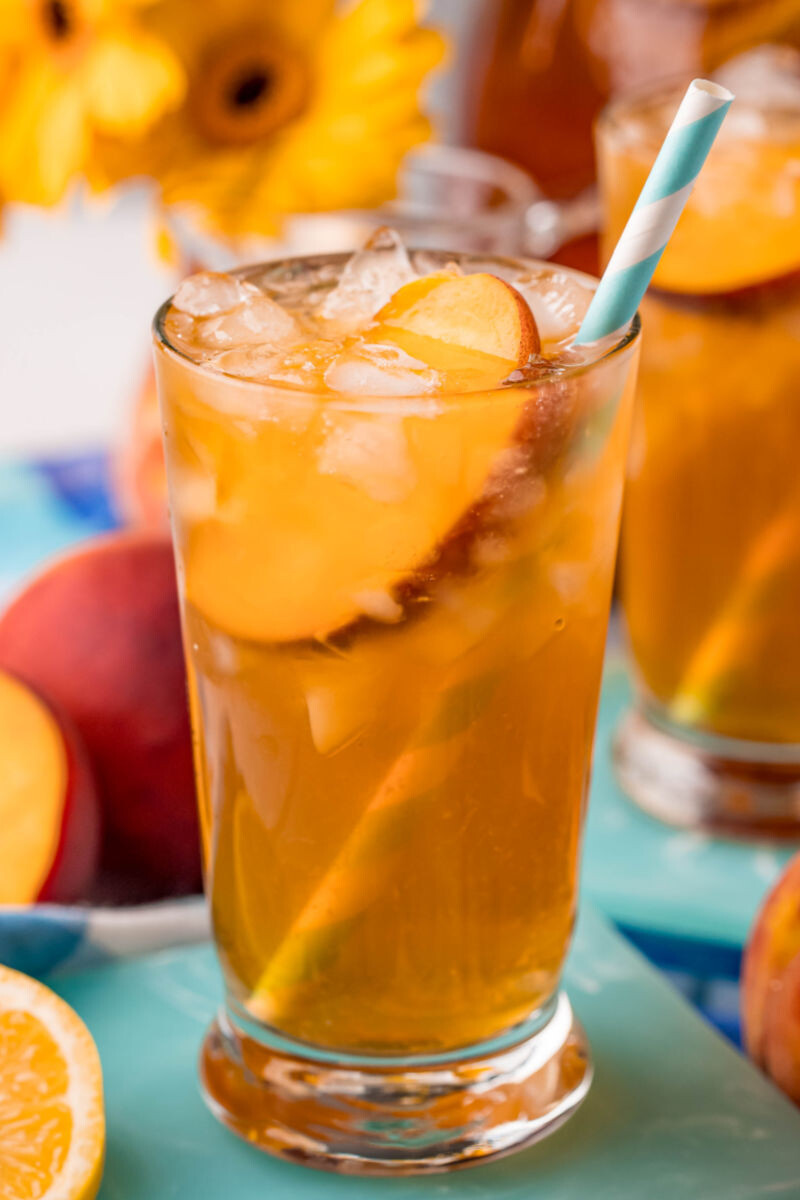 close up of a glass of peach sweet tea with a straw