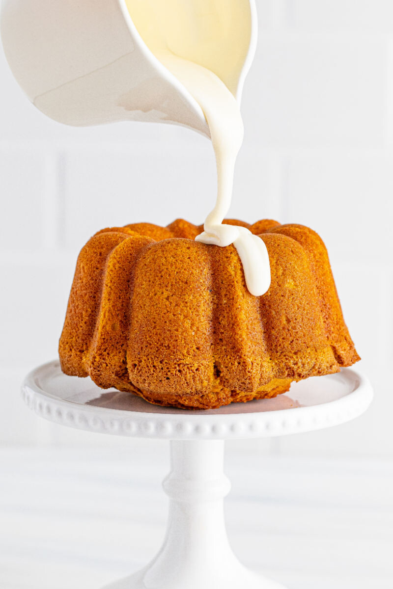 cream cheese glaze being poured over the top of a pumpkin bundt cake