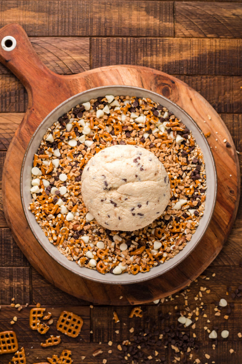 chilled cheese ball on a bowl of chocolate chips, white chocolate chips, toffee bits, chopped pretzel, and walnuts