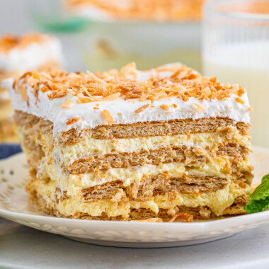 square image of a slice of coconut icebox cake on a plate with a sprig of mint