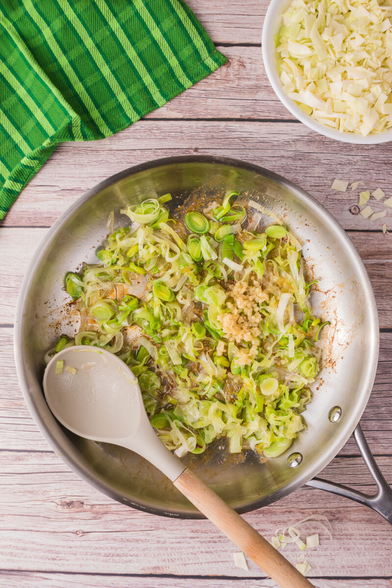 sauteed leeks and garlic in a skillet next to a bowl of shredded green cabbage