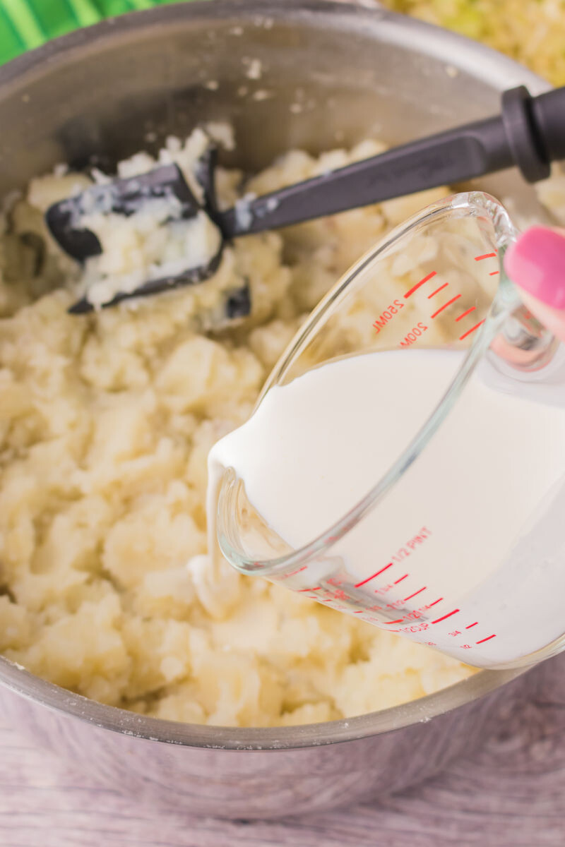 heavy cream being added to mashed potatoes in a pot