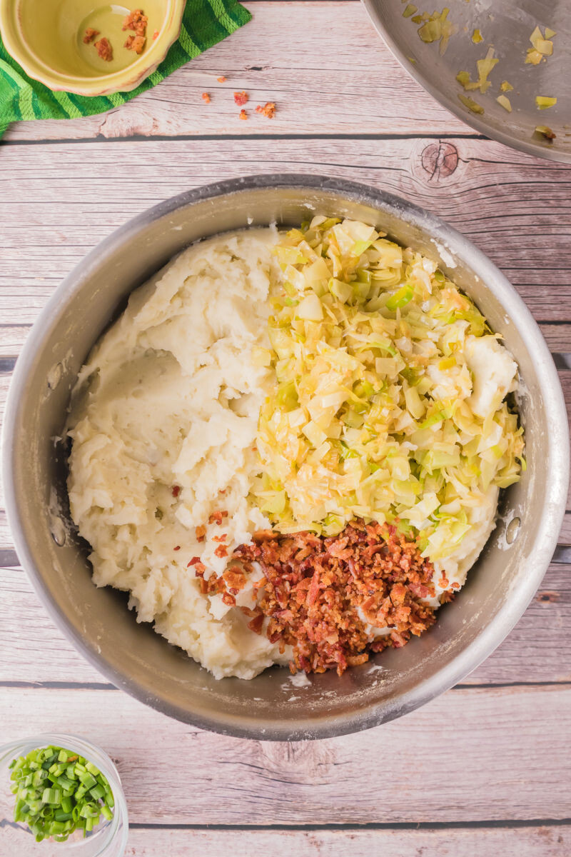 crumbled bacon and leek/cabbage mixture added to mashed potatoes in a pot