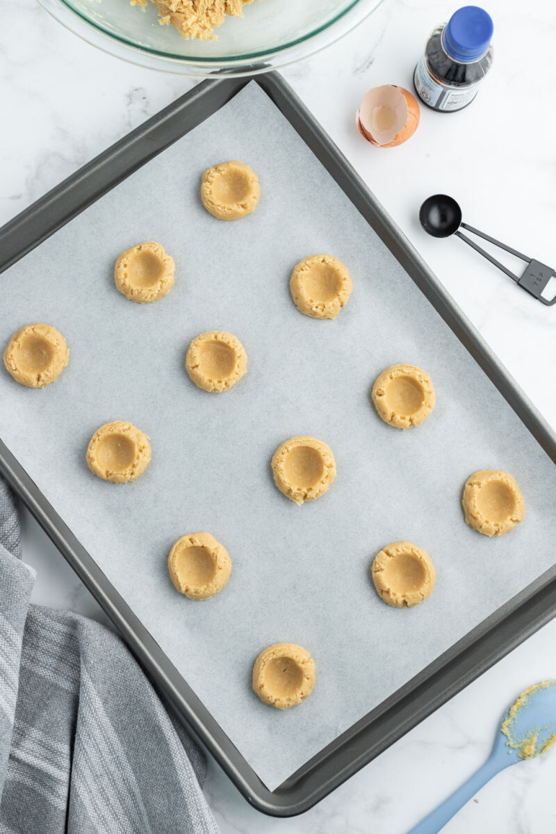 cookie dough balls on a baking sheet with indents pressed into the top of each cookie