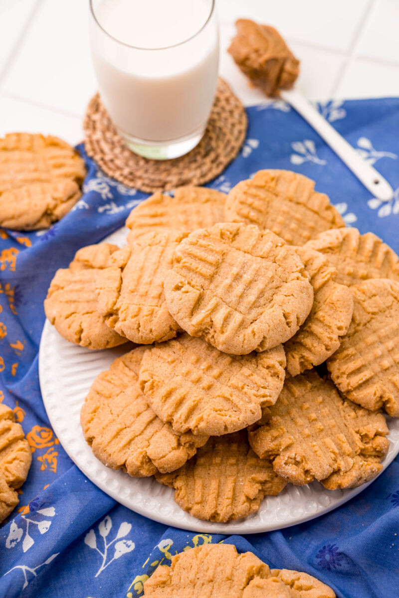 side view of peanut butter cookies on a plate next to milk and a spoon of peanut butter