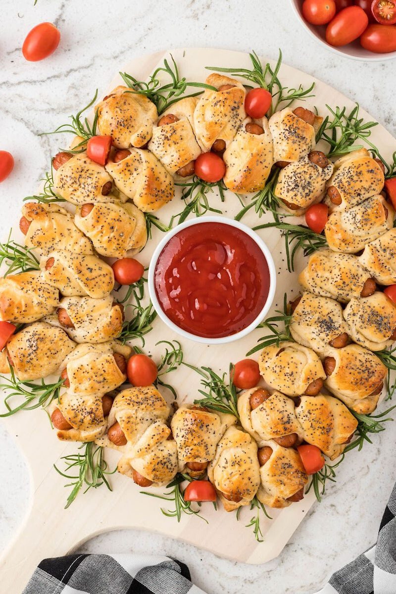 pigs in a blanket wreath on a pizza peel with a bowl of ketchup in the center