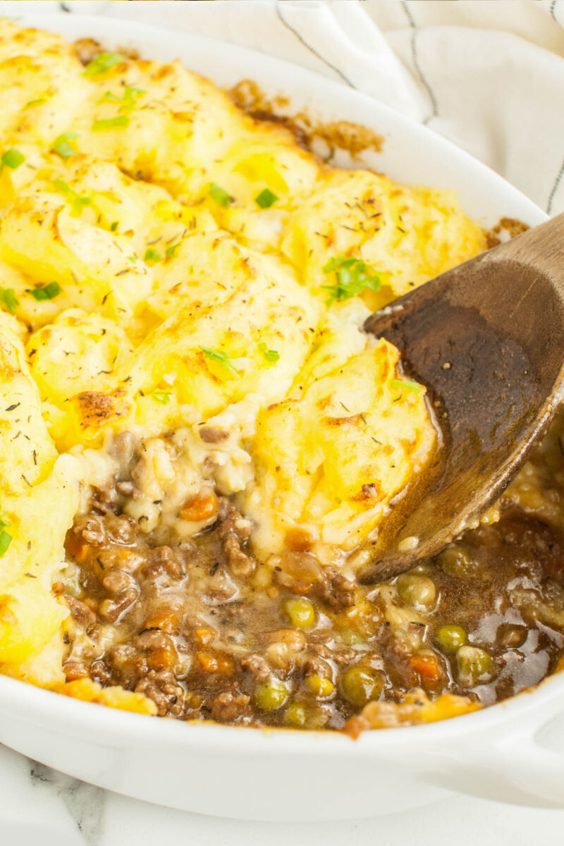 wooden spoon in a dish of shepherd's pie with a portion taken out to show the beef and gravy filling