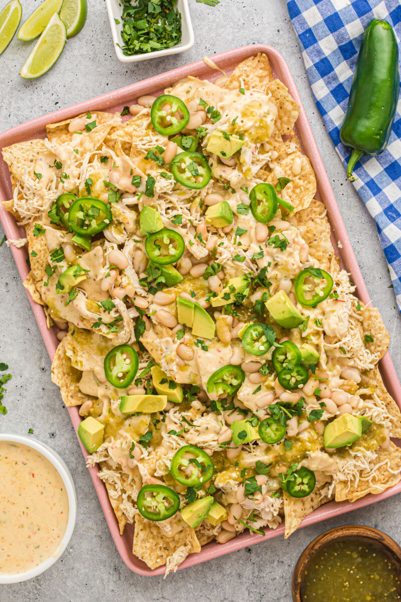 queso blanco chicken nachos on a bakign sheet next to limes, slsa verde, and queso blanco