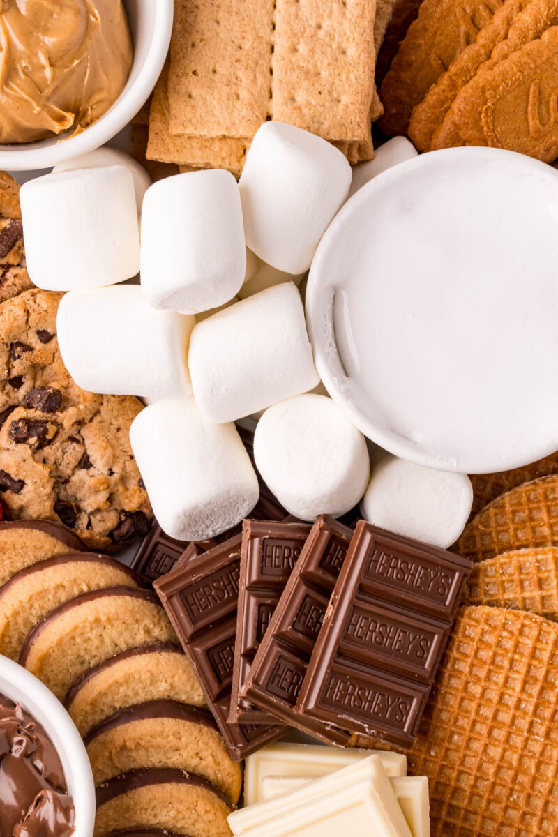 close up of chocolate bar pieces, bowl of marshmallow fluff, marshmallows, and cookies on a platter