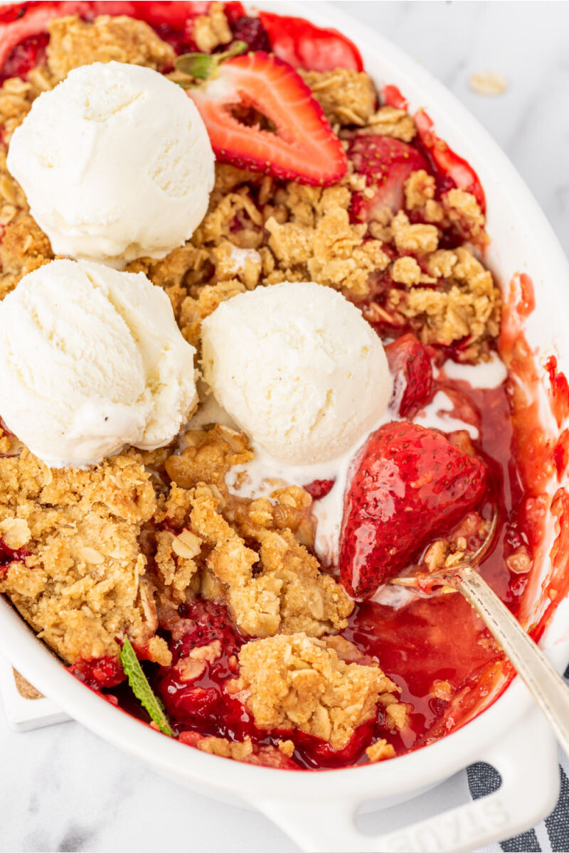 close up of a serving spoon with a strawberry in a dish of strawberry crisp
