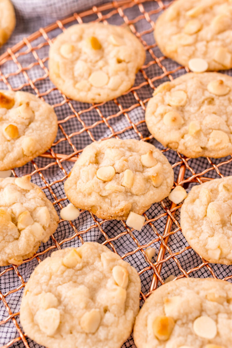 side view of white chocolate chip macadamia nut cookies on a wire rack with nuts sprinkled around