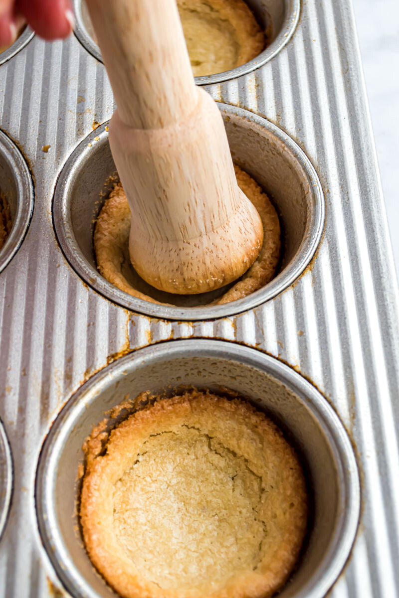 tart tampers pressing indents into baked sugar cookies in a muffin tin