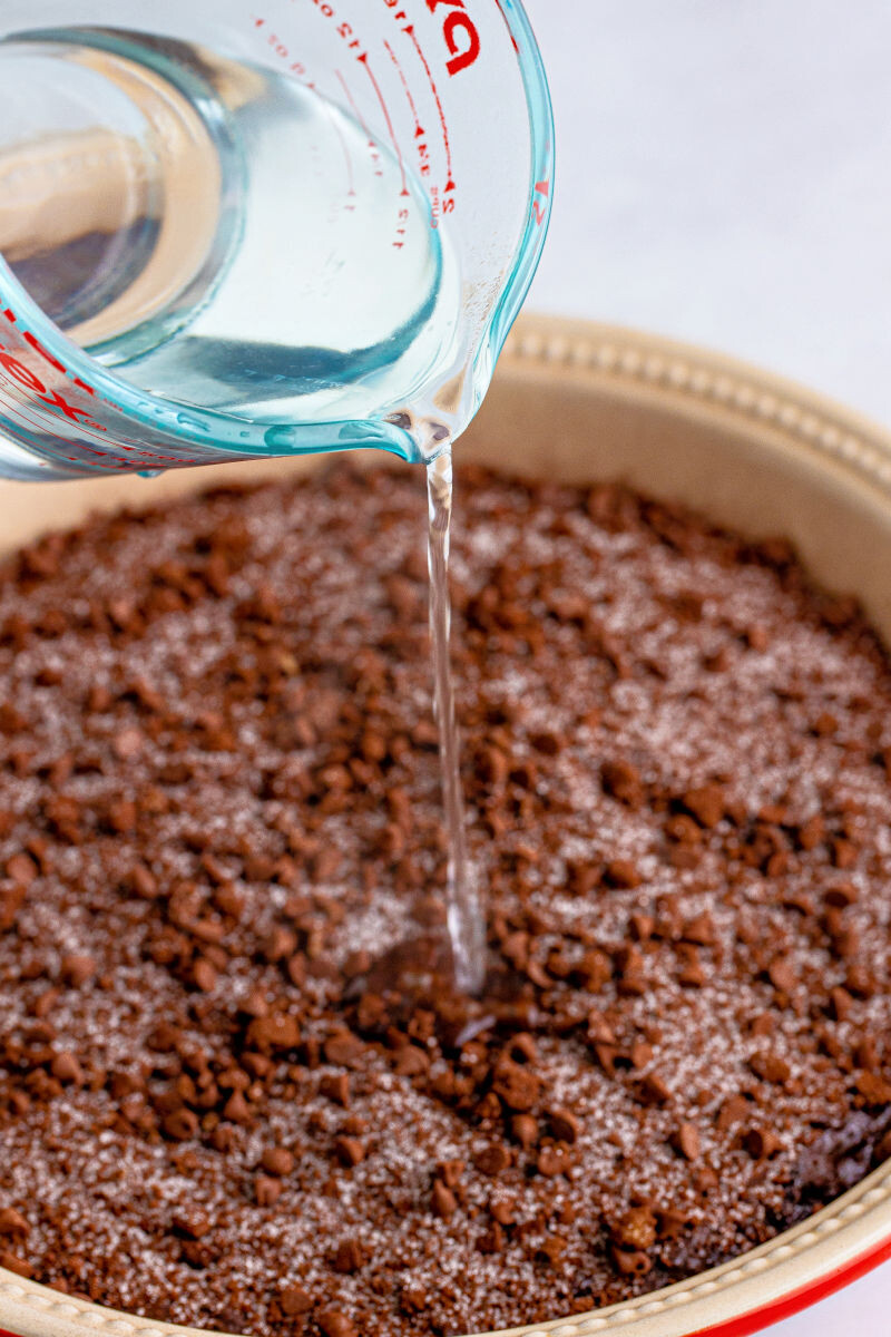 boiling water being poured over chocolate cake abtter topped with sugar and cocoa powder mixture