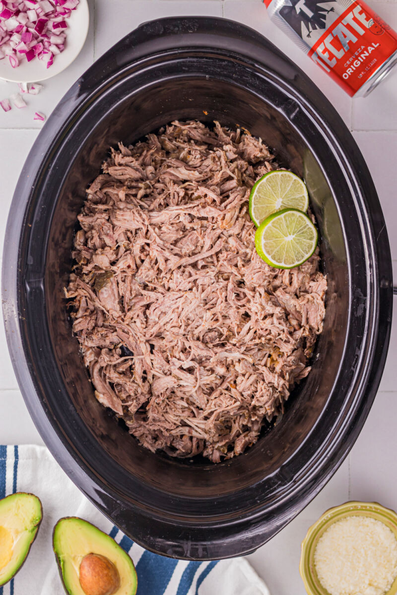 shredded slow cooker carnitas in a crock pot with two slices of lime