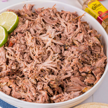 square image of slow cooker carnitas in a serving bowl with lime slices for garnish