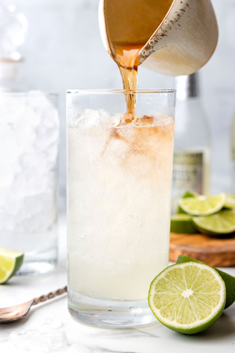 dark rum being poured over ginger beer and lime juice in an ice filled glass