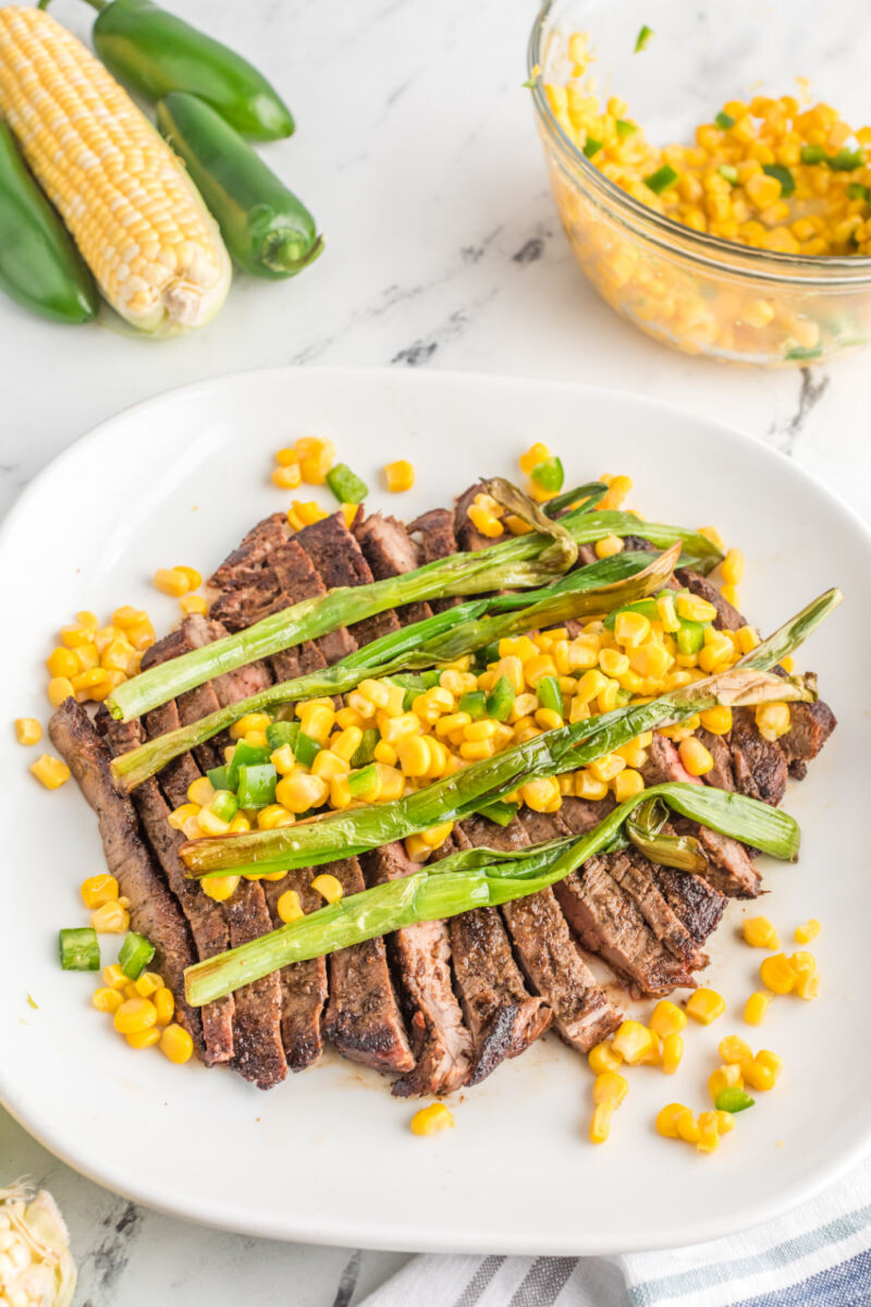 sliced flank steak topped with corn salsa and charred green onions on a plate