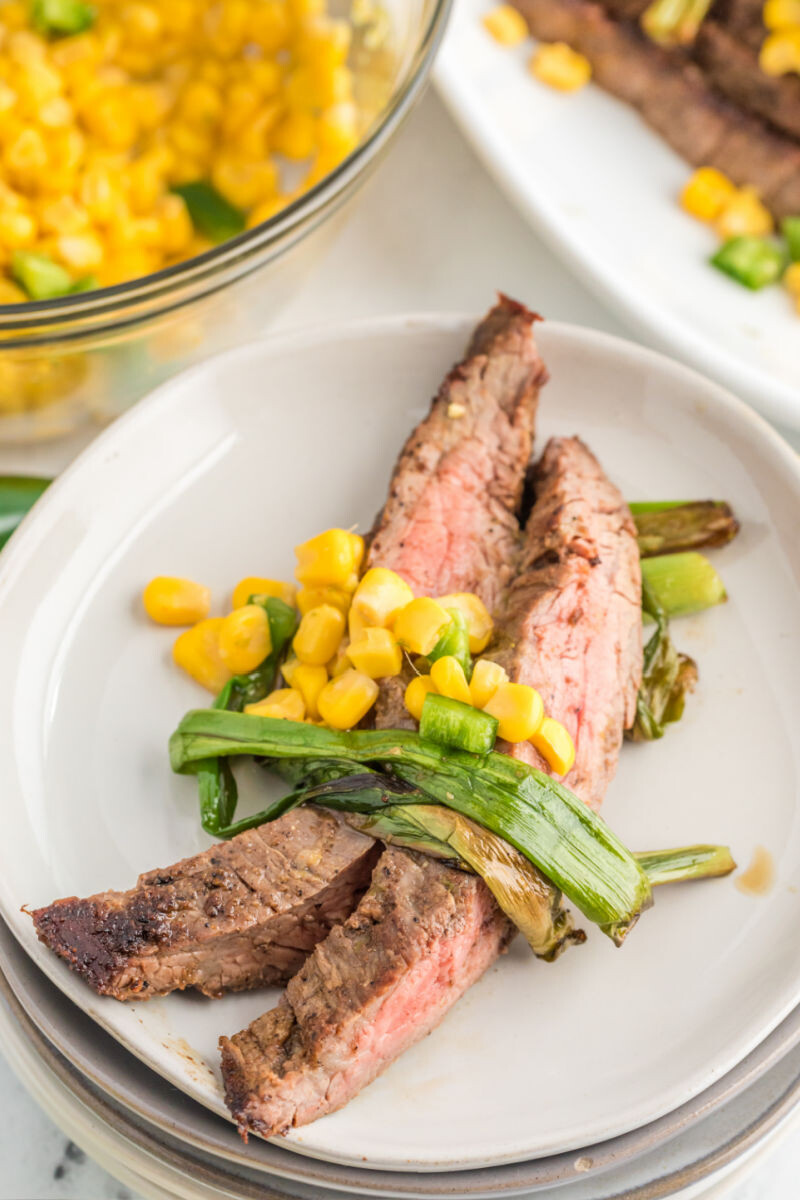 two slices of flank steak, corn salsa, and wilted scallions on a plate