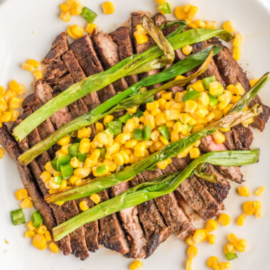 square image of sliced flank steak topped with corn salsa and charred scallions on a plate