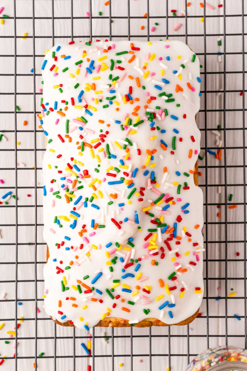 vanilla icing and rainbow sprinkles on a loaf of ice cream bread on a wire rack