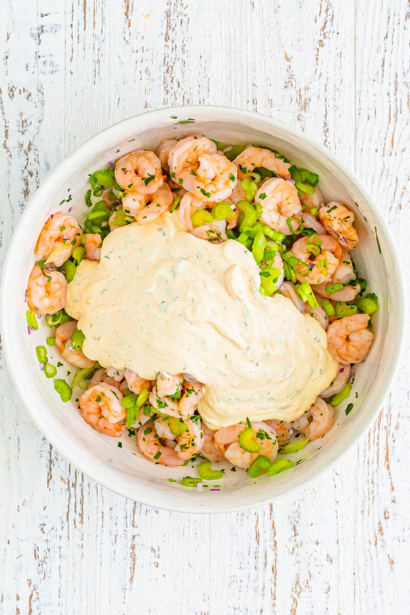 dressing poured over shrimp salad ingredients in a mixing bowl