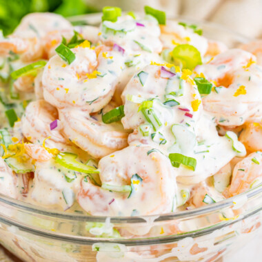 square image of shrimp salad in a glass bowl with green onion on top for garnish