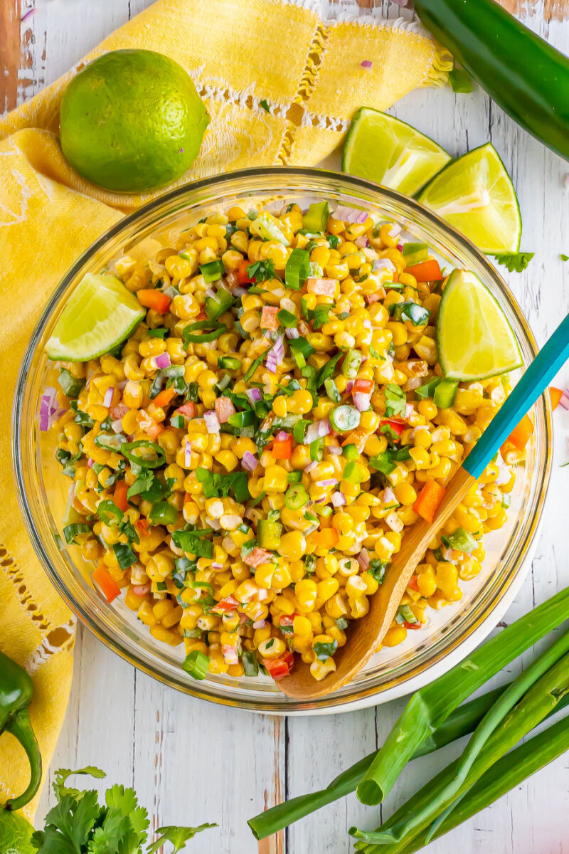looking down at tex-mex corn salad in a serving bowl surrounded by limes and green onion